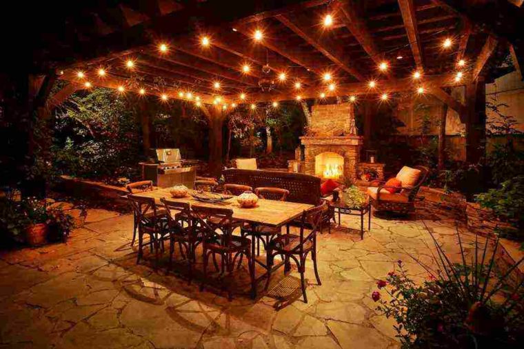 terrasse éclairage idée guirlande lumineuse salon de jardin fauteuil table à manger chaise bois design pierre